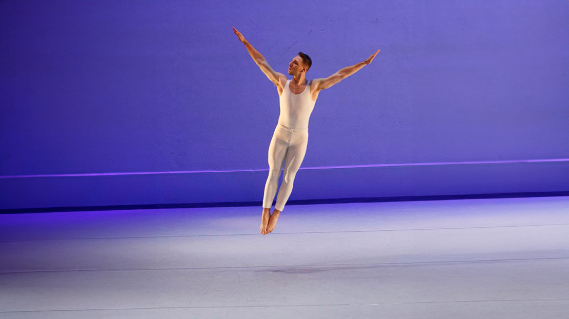 One dancer soars through the air with arms extended and legs in a tight parallel assemblé in Aureole, choreographed by Paul Taylor.