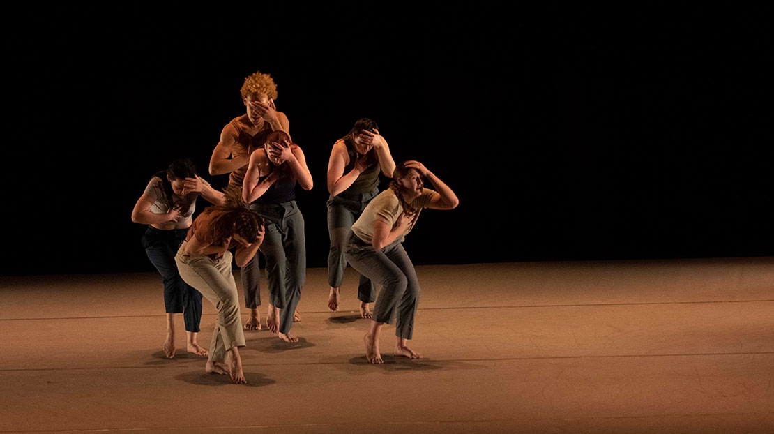 Six dancers stand crouched clutching their heads and chests in And still, they move, a contemporary dance piece choreographed by Webster Dance faculty member Xi Zhao.