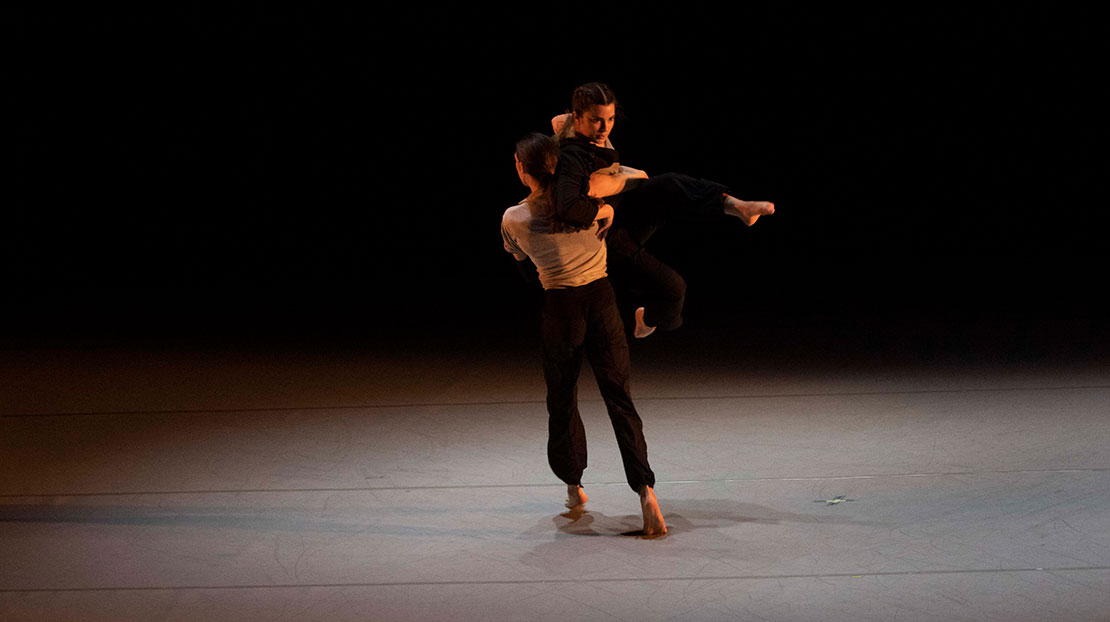 One dancer lifts another who extends their leg forward in Decode, choreographed by Maggi Dueker.