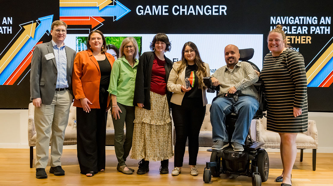 Group of attendees stand with Katie Fields on stage in front of screen that reads "Game Changer."