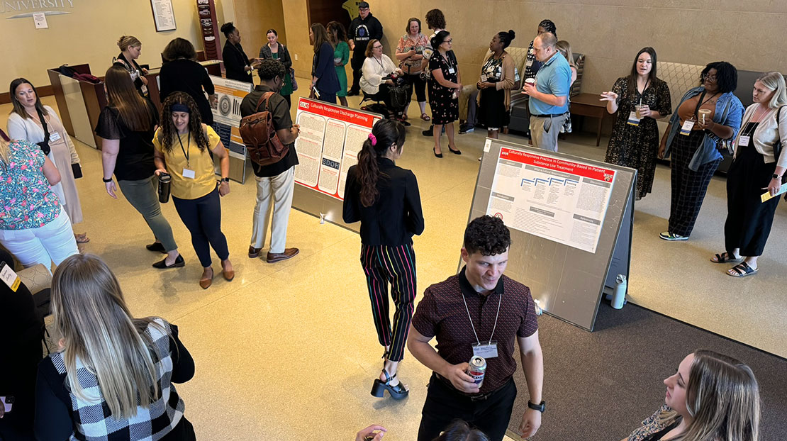 Research posters in middle of room with lots of people milling about looking at posters and talking.