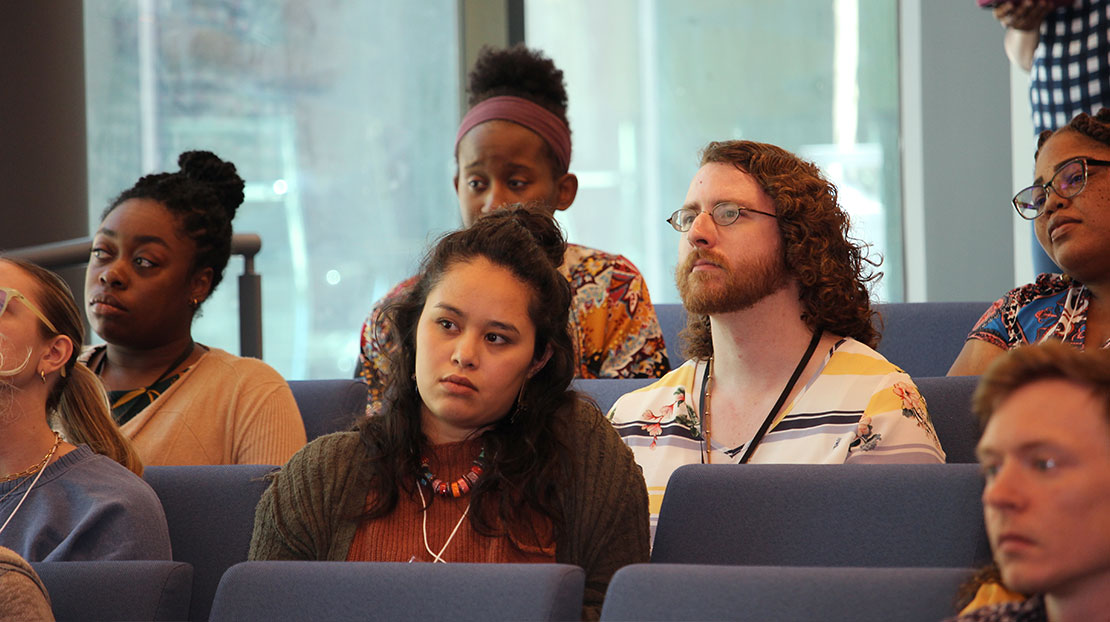 Diverse group of students sitting in auditorium seats attentively listening.