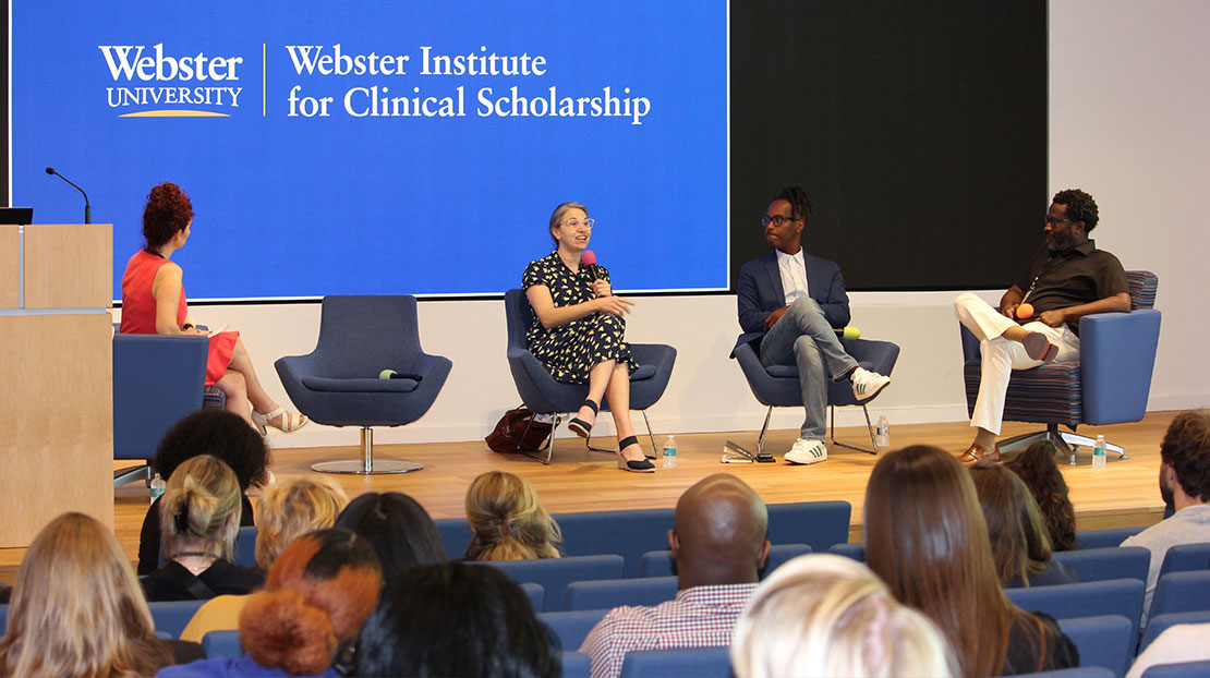 Panel of speakers sit on stage in front of audience.