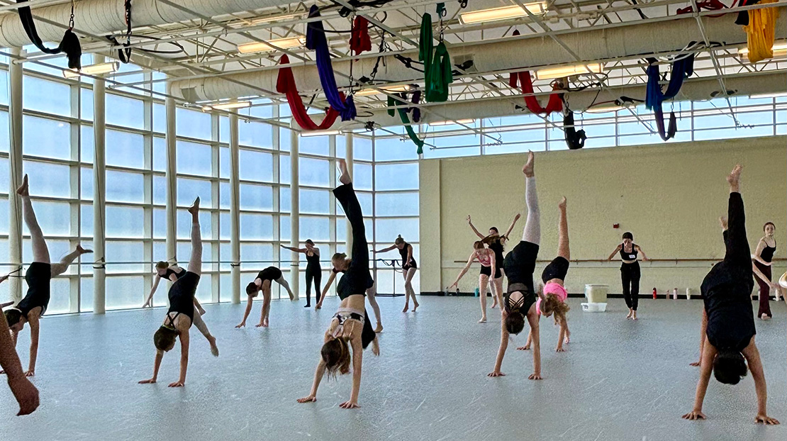 Dancers perform an inversion with hands on the floor and left leg extended upward in a modern dance combination taught by Webster Dance instructor Emily Haussler.