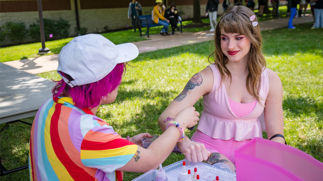 An artist painting an airbrush tattoo onto a Webster student.