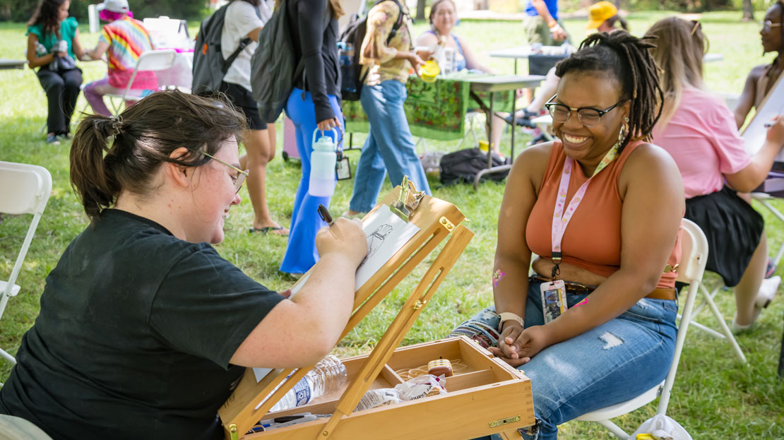 A Webster student smiles as they have their caricature drawn by an artist. 