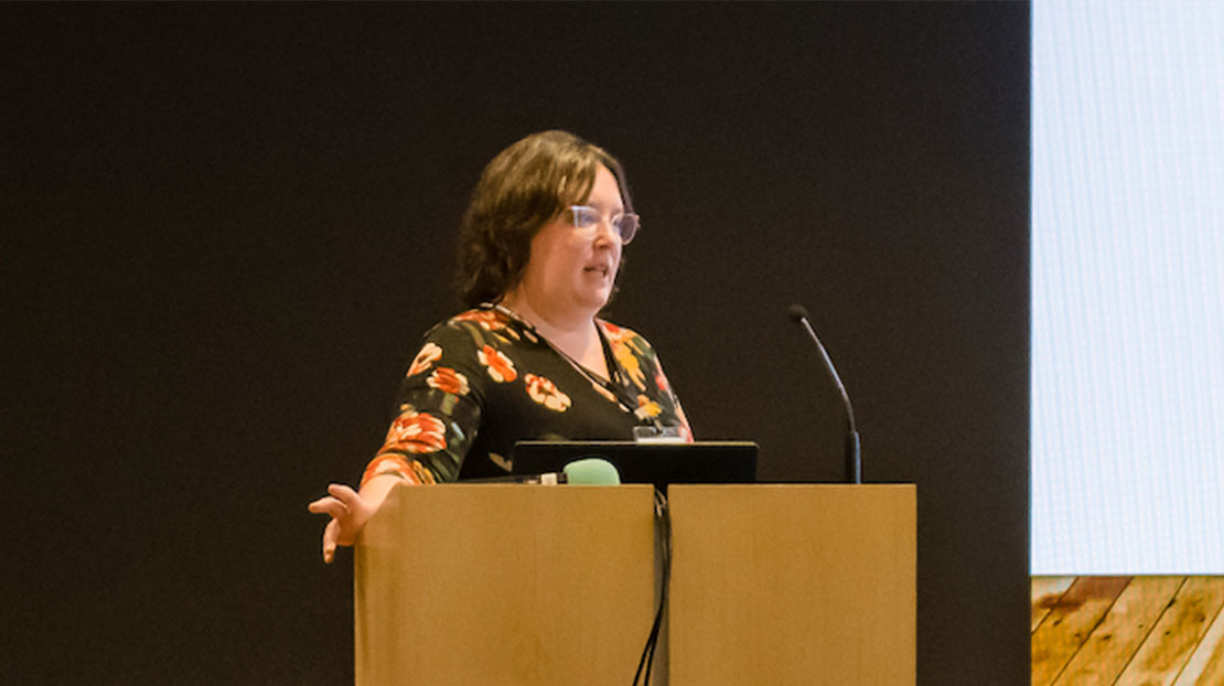 Student gives presentation while standing and resting open hand on corner of a wood podium.