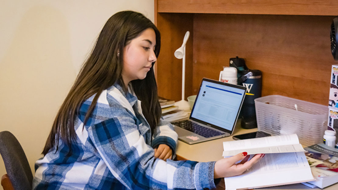 A Webster student working at their desk in their dorm room.