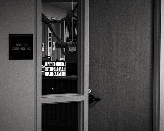 A black and white photo of a school counseling office door with a sign that reads "Make It A Great Day" in a lightbox.