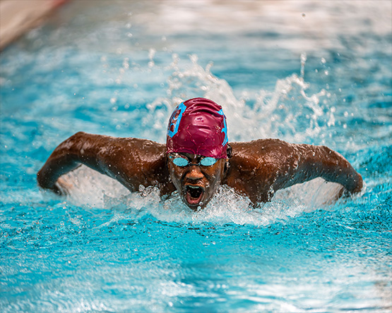 A swimmer wearing a swim cap and goggles is performing a butterfly stroke. They are currently taking a breath mid-stroke.