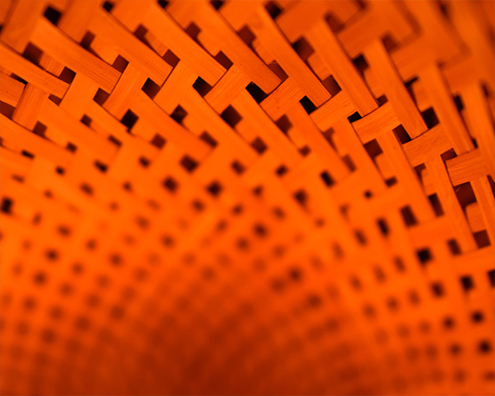 A close-up of an orange, weaved material, creating a repeating pattern of small, square shapes. The image is slightly blurred, adding to the abstract and textured feel.