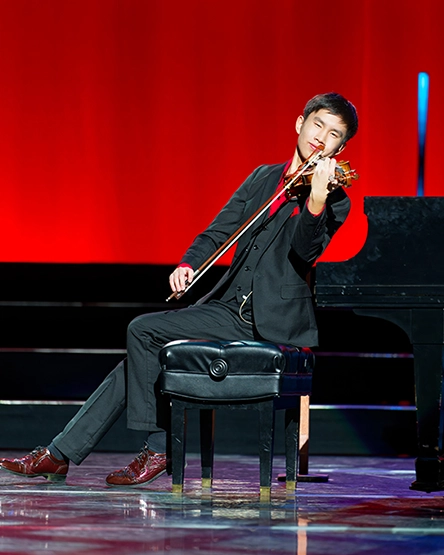 asher koh sitting on piano bench playing violin