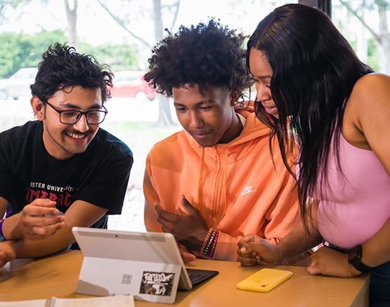 Three students studying a laptop screen together 